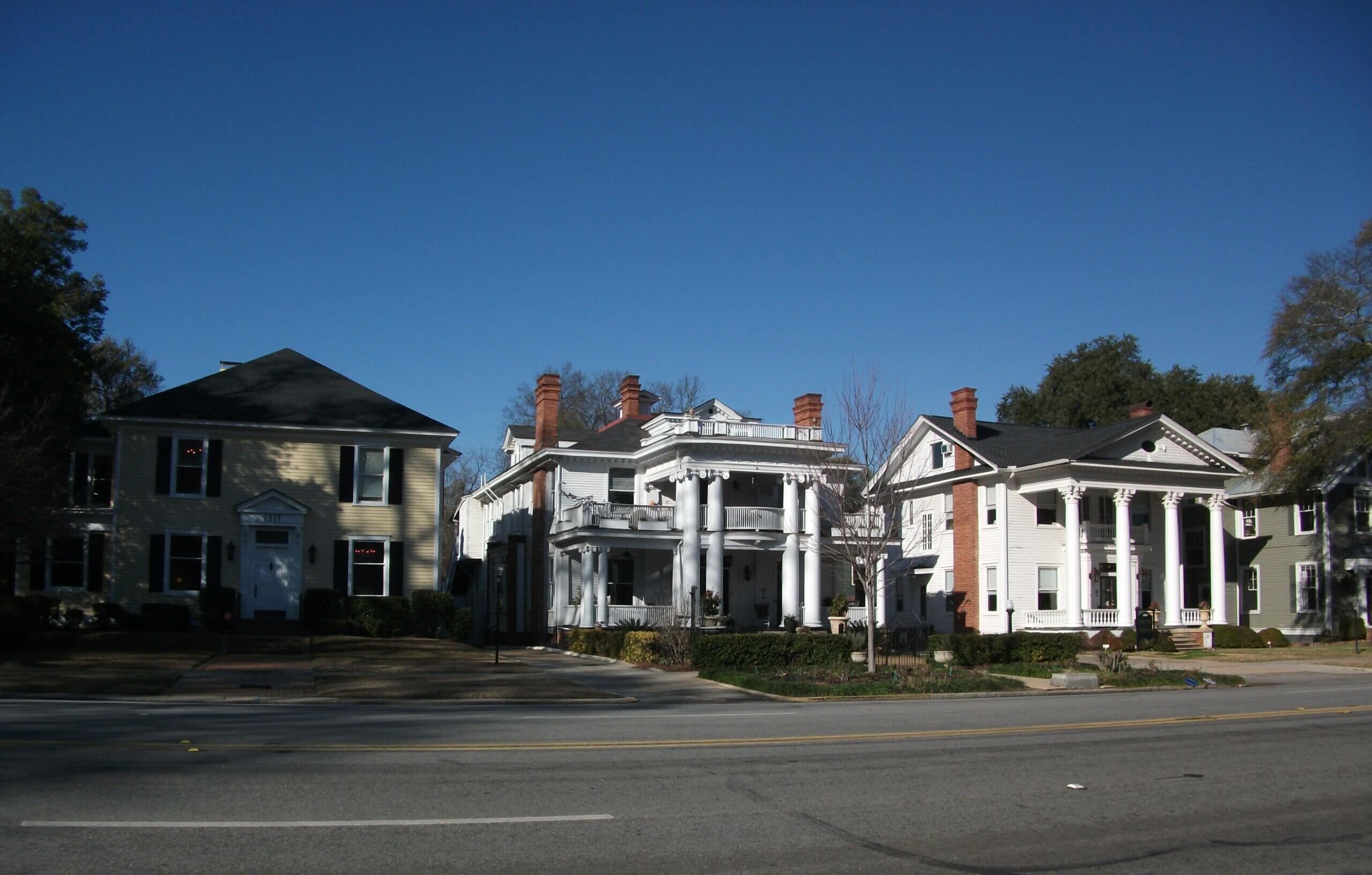 Photograph of a street with two story homes, two of which have large columns on the front facade