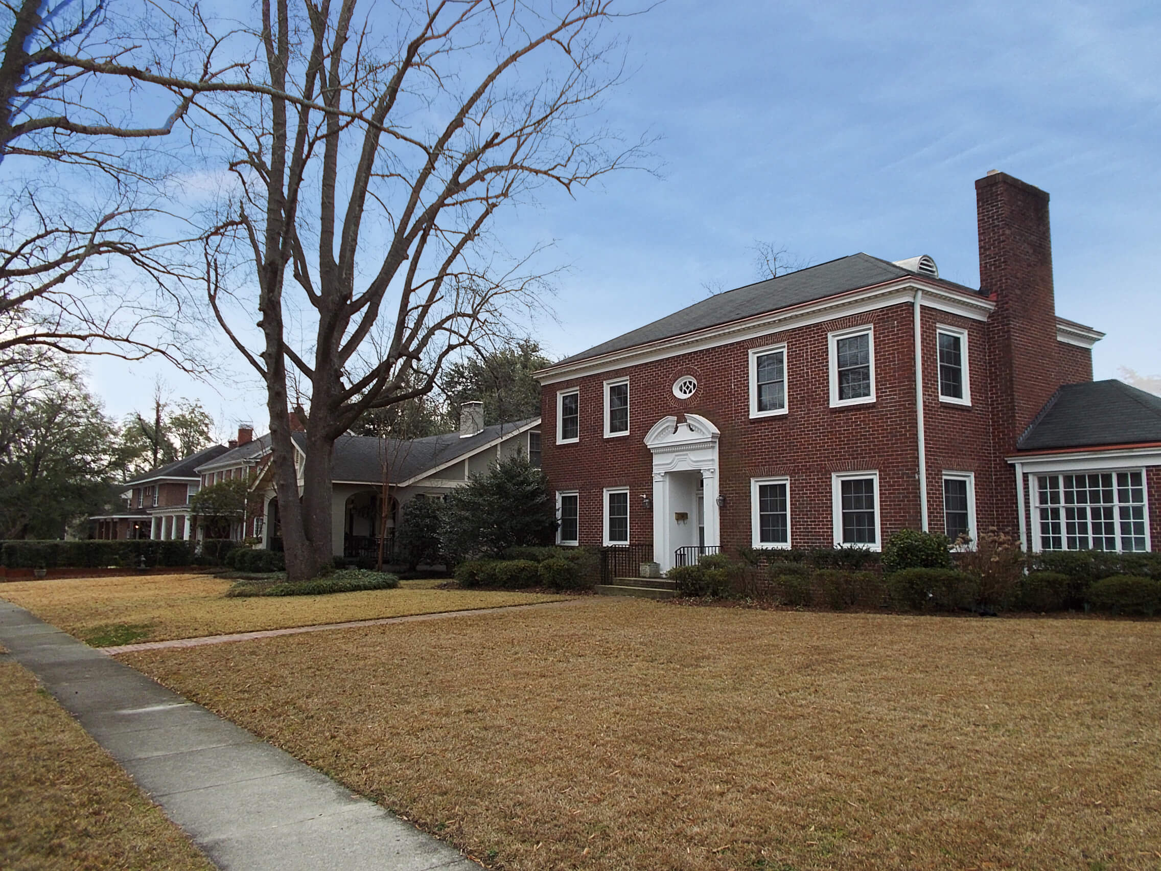 Photograph of a two story brick home in the foreground, with other brick homes in the rear