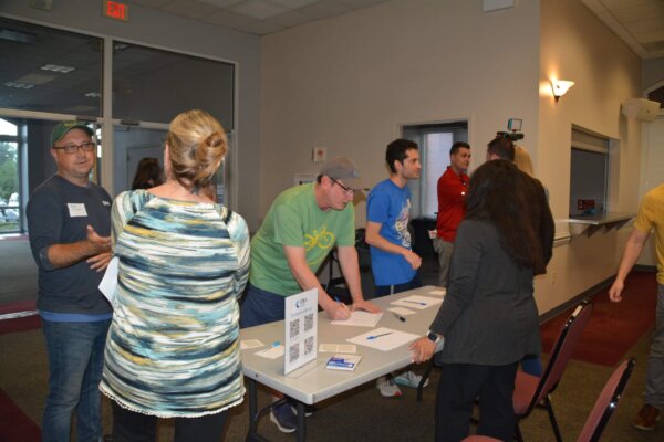 A photo of people chatting and signing in at a sign in table at the entrance to the design workshop.