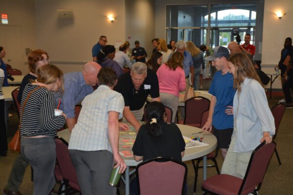 A photo of individuals gathered around multiple circular tables with maps at the design workshop.