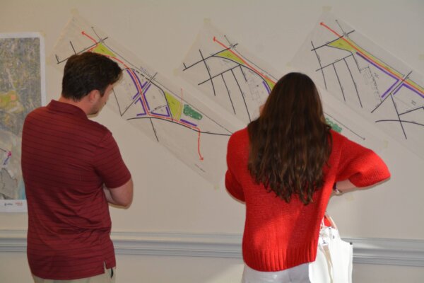 Individuals stand and review the early concepts explored in response to day 1 of the design workshop, which are taped to the wall