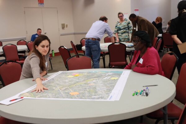 A photo of individuals gathered around tables with maps at the design workshop.