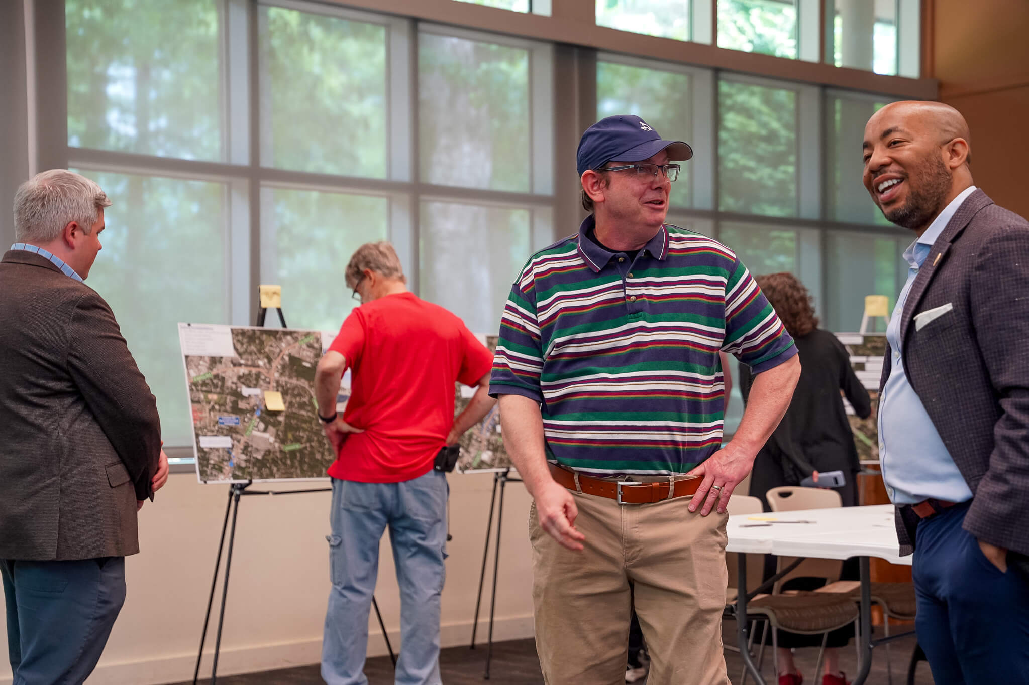 participants at a public open house chat in the foreground, while others in the background look at boards placed on easels with sticky notes affixed. The meeting is at the Virginia Bedford Center at Earlewood Park