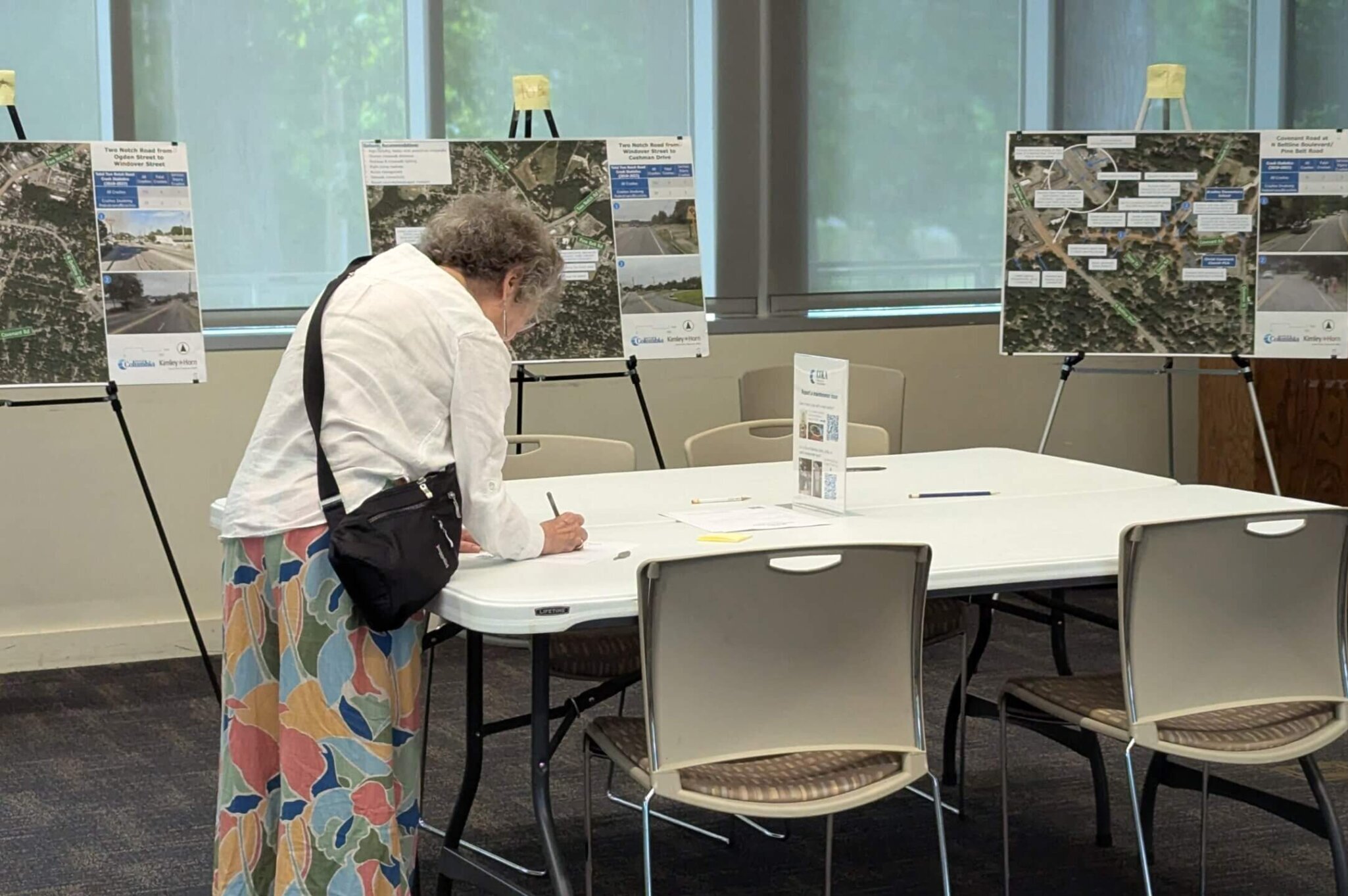 photograph of a woman filling out a comment form at a table with meeting boards in the background